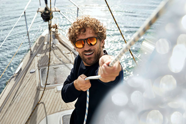 Man wearing mirrored lenses stood on a boat holding the rigging